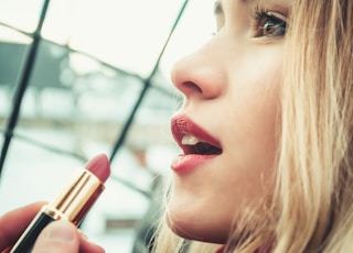 selective focus photography of woman holding lipstick