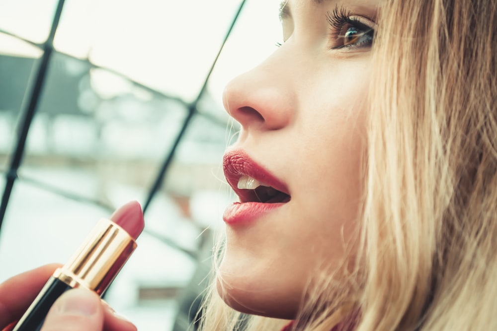 fotografia a fuoco selettiva di donna che tiene il rossetto