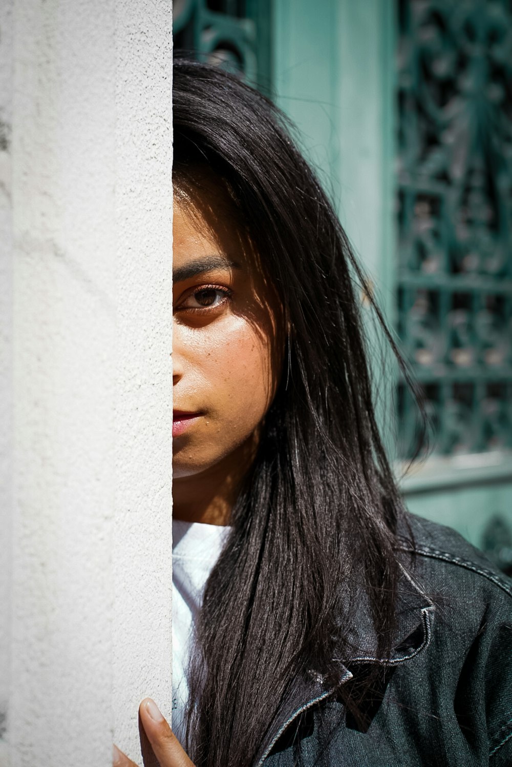 a woman with long black hair standing behind a wall