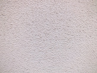 Close-up of a freshly finished stucco wall with a smooth, creamy texture under natural sunlight.