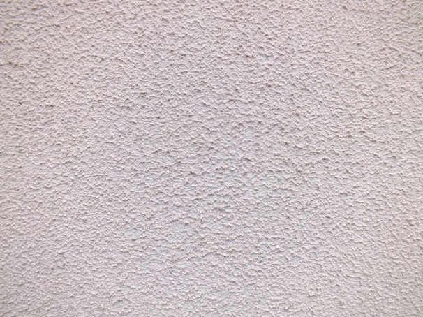 Close-up of a freshly finished stucco wall with a smooth, creamy texture under natural sunlight.