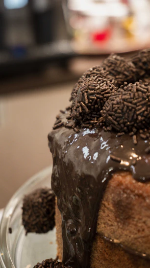 A close-up of a freshly baked chocolate cake with glossy frosting and sprinkles on top.