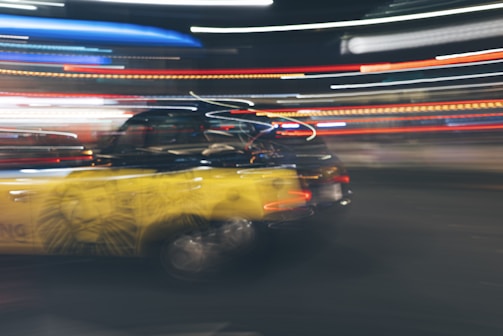 A dynamic scene features a black and yellow taxi with motion blur, suggesting speed. Neon lights streak across the background, enhancing the sense of movement and urban energy.