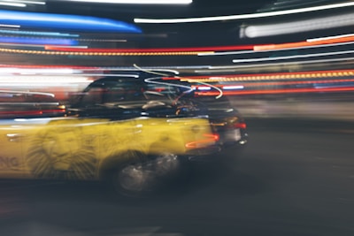 A dynamic scene features a black and yellow taxi with motion blur, suggesting speed. Neon lights streak across the background, enhancing the sense of movement and urban energy.