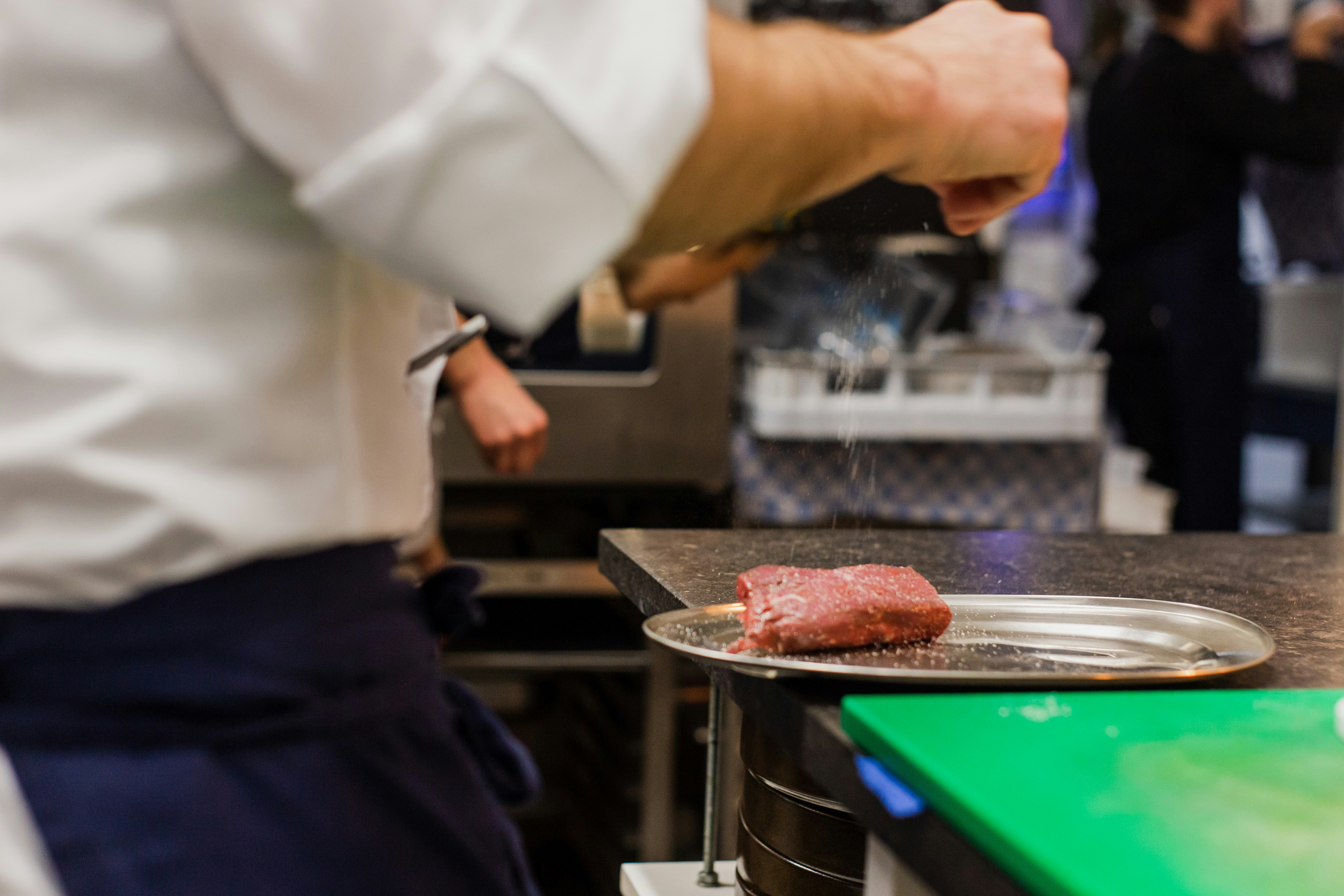Chef handling a tray of raw meat in a restaurant kitchen