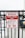 A metal fence with a red and white warning sign stating 'Permit Parking Only.' It indicates unauthorized vehicles will be towed at the owner's expense, with towing enforced at all times. There is a graphic of a tow truck and a car beneath the text. Some graffiti is visible on the sign.