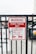 A metal fence with a red and white warning sign stating 'Permit Parking Only.' It indicates unauthorized vehicles will be towed at the owner's expense, with towing enforced at all times. There is a graphic of a tow truck and a car beneath the text. Some graffiti is visible on the sign.