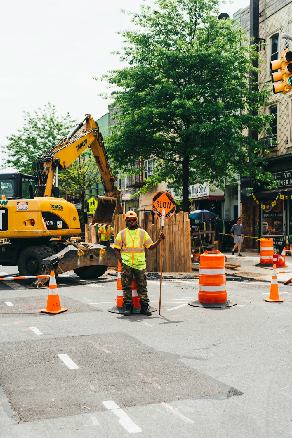 man wearing green reflective vest standing near traffic cones and backhoe