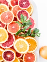 A vibrant arrangement of citrus fruits and green leaves on a clean white surface, highlighting freshness.