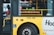 A yellow city tour bus has a digital sign indicating it is not in service. A person in a reflective vest can be seen inside the bus, near the door. Various signs about accessibility and passenger instructions are visible on the bus.