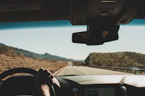 Close-up of hands gripping a steering wheel with a scenic desert road ahead.