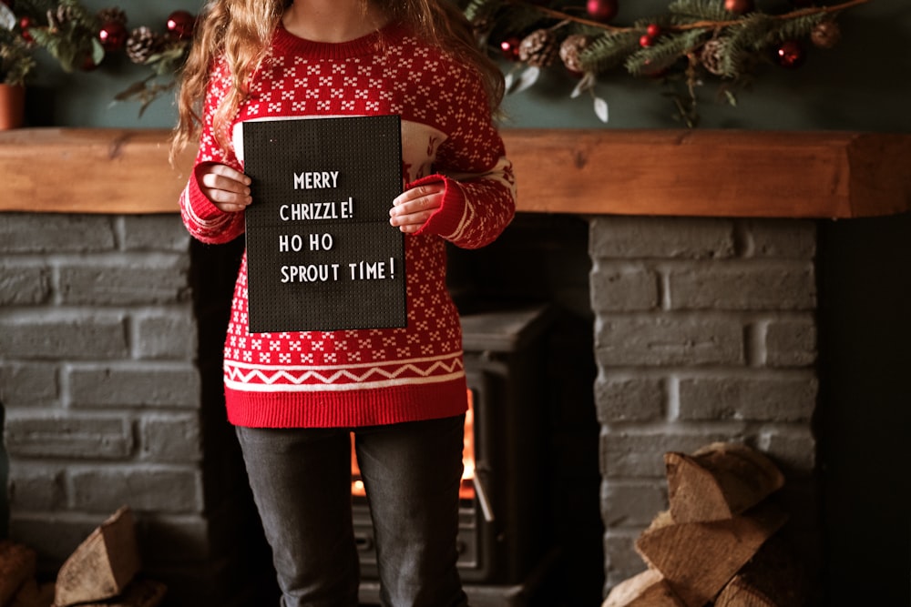 woman wearing red and white crew-neck sweater holding paper with print standing near fireplace