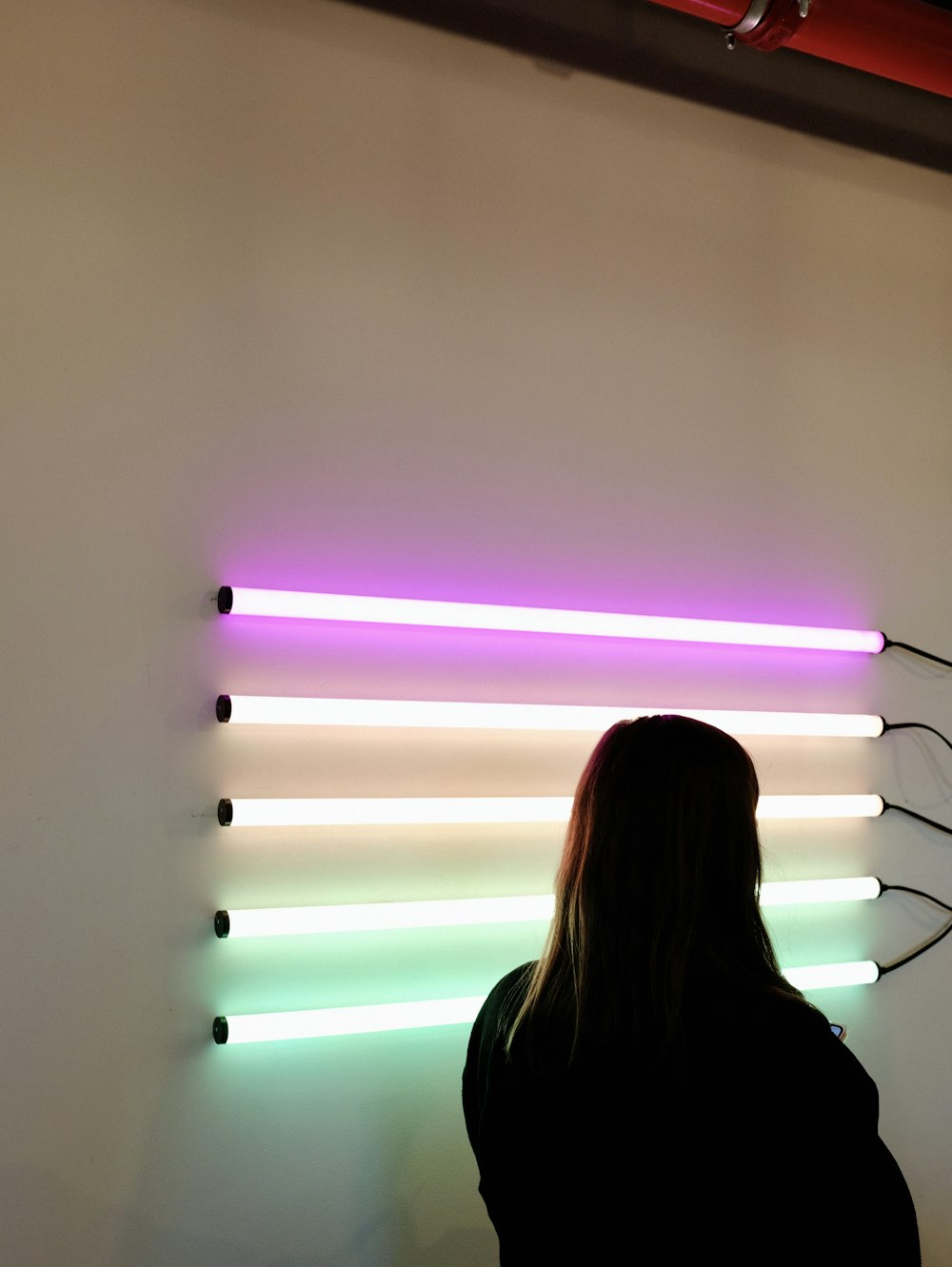 Frau neben der Wand mit eingeschalteten Leuchtstoffröhren in verschiedenen Farben