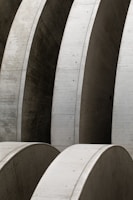 Massive concrete arches with smooth surfaces, arranged in a repetitive pattern, create a sense of industrial architecture. The structures display meticulous craftsmanship and structural integrity with clean lines and subtle texture variations.