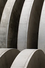 Massive concrete arches with smooth surfaces, arranged in a repetitive pattern, create a sense of industrial architecture. The structures display meticulous craftsmanship and structural integrity with clean lines and subtle texture variations.