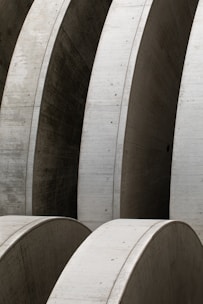 Massive concrete arches with smooth surfaces, arranged in a repetitive pattern, create a sense of industrial architecture. The structures display meticulous craftsmanship and structural integrity with clean lines and subtle texture variations.