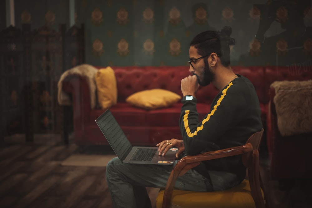 man sitting on wooden chair while using laptop computer on lap