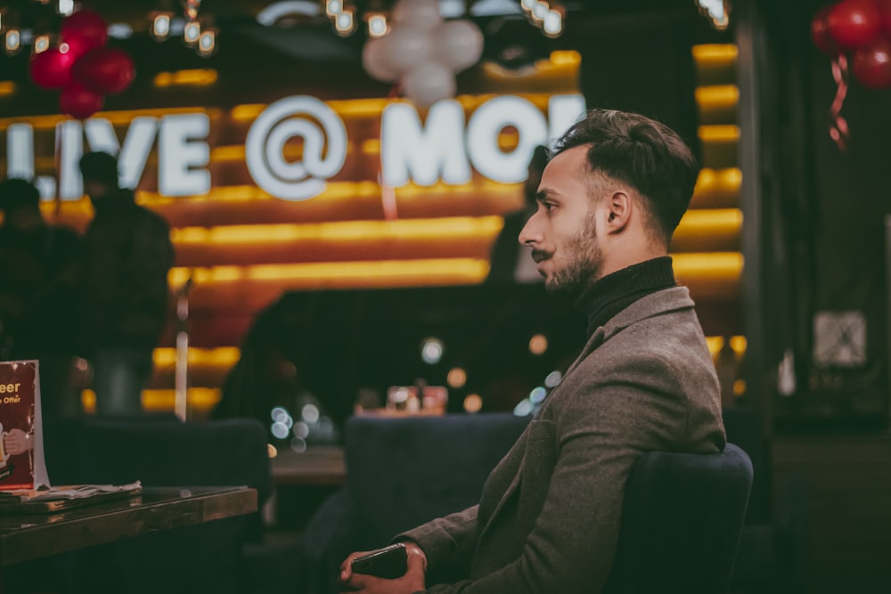 man sitting on chair beside table while wearing brown blazer