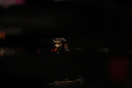 A dark, moody shot of a grotesque, detailed horror mask illuminated by subtle red lighting.