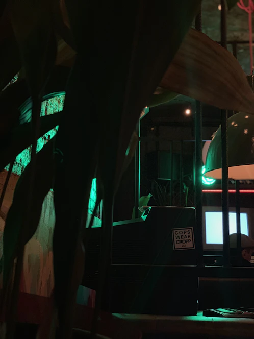 A vintage computer with a glowing green screen sits on a wooden desk, bathed in warm ambient light.