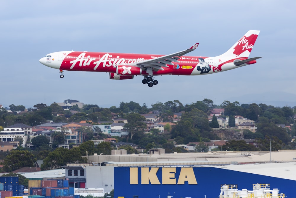 白と赤のエアアジアの旅客機が昼間、イケアの建物上空を飛ぶ