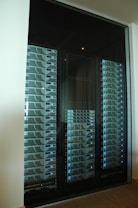A server room or data center featuring several racks of network servers with blue indicator lights. The setup is organized and enclosed within a glass cabinet.