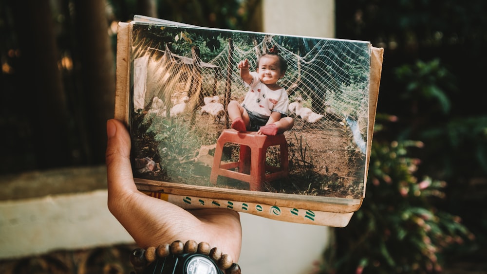 Person, die ein Foto eines Babys auf dem Stuhl hält