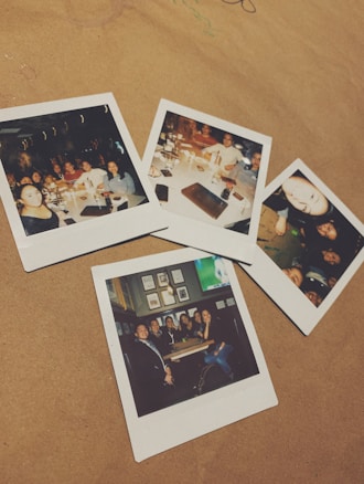 Five polaroid photographs are laid out on a tan surface. Each photo features groups of people at various social gatherings, seemingly enjoying themselves at restaurants or bars. The photos contain friends or family smiling, posing together, and sharing meals and drinks.