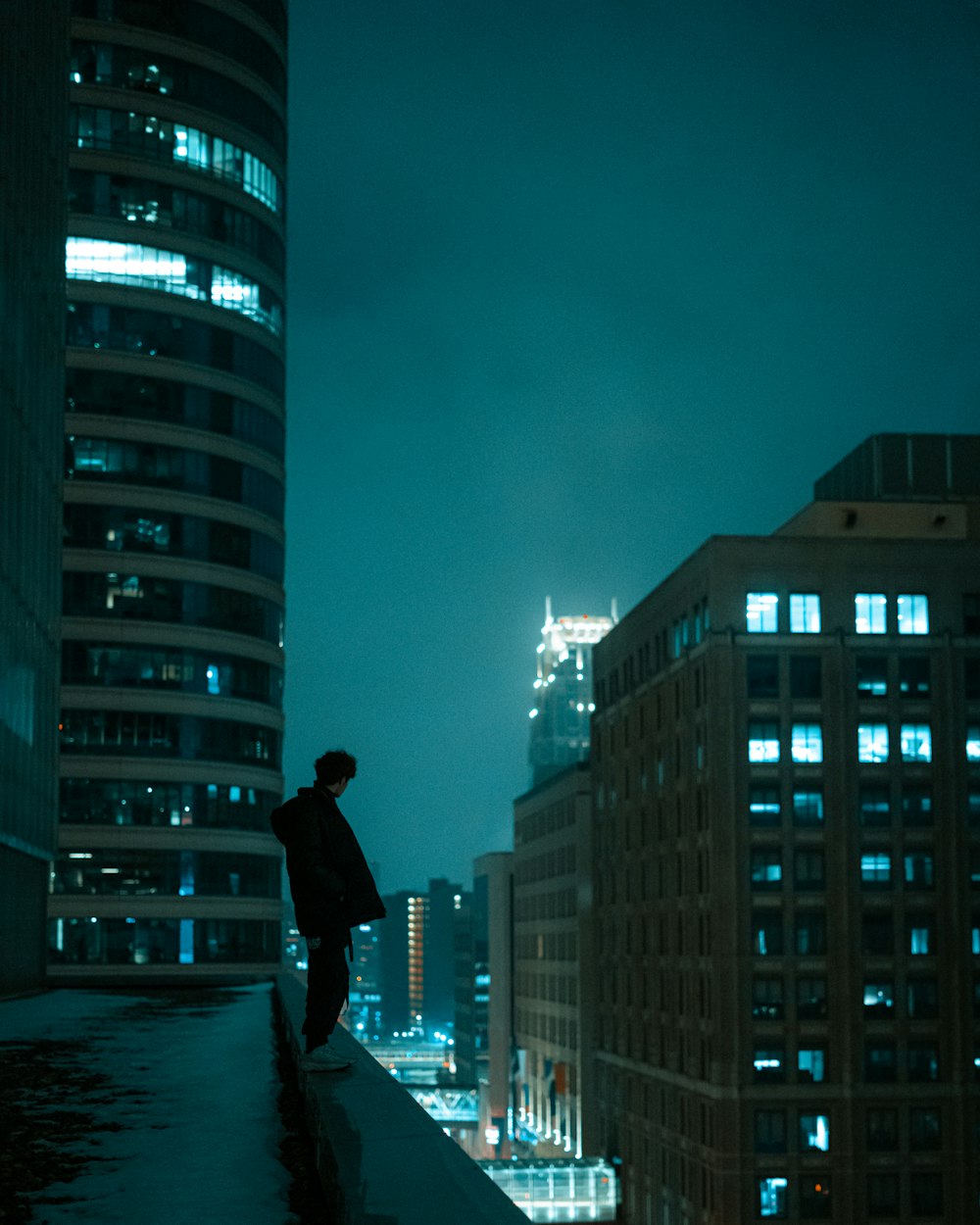 man standing on rooftop viewing city with high-rise buildings during night time