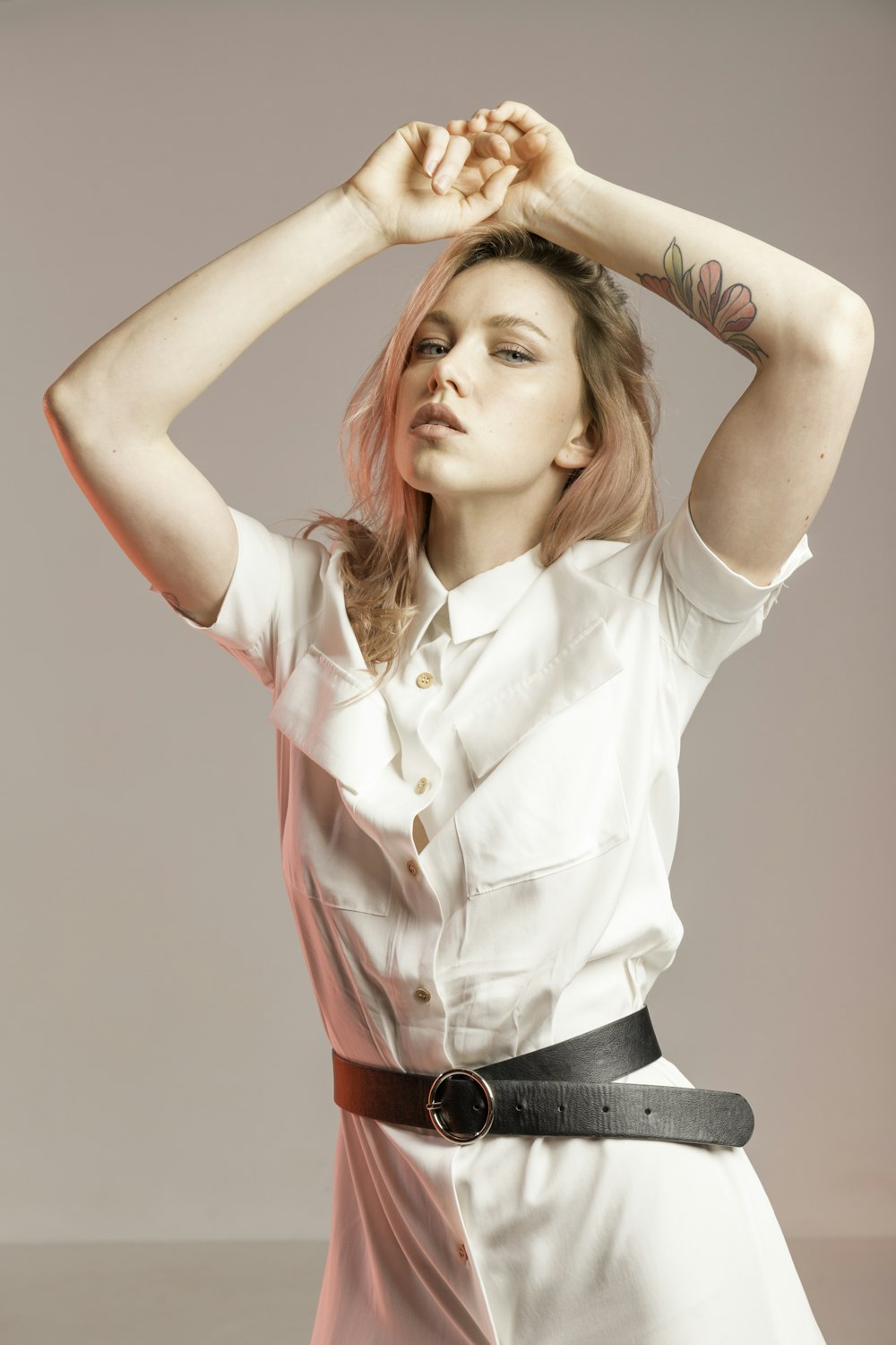 woman wearing white collared button-up dress standing while putting both hands on her head