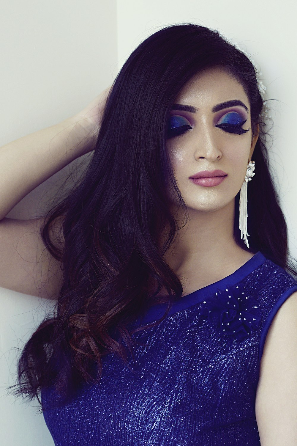 woman wearing blue sleeveless blouse with blue eyeshadow standing while touching her hair