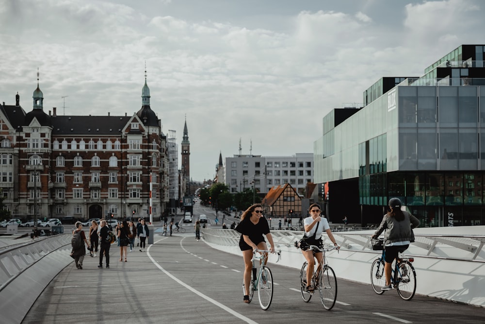 two people biking and other people walking on pathway near buildings under white and blue sky