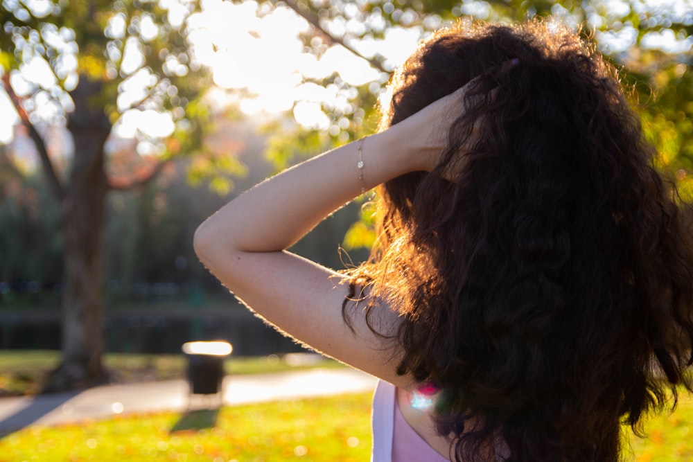 woman touching her hair while standing surrounded with green trees