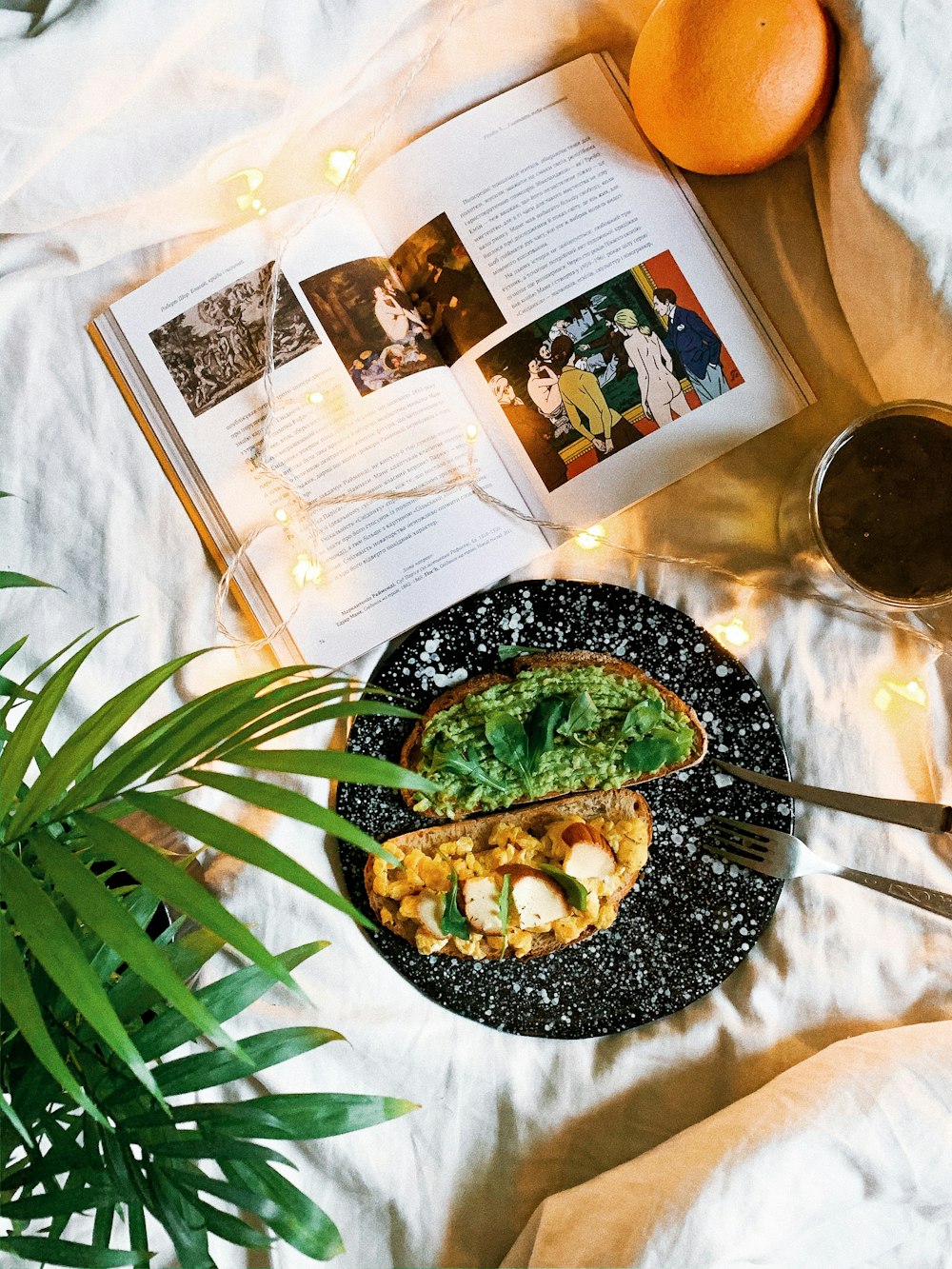 open book near bread with guacamole on top and glass of coffee