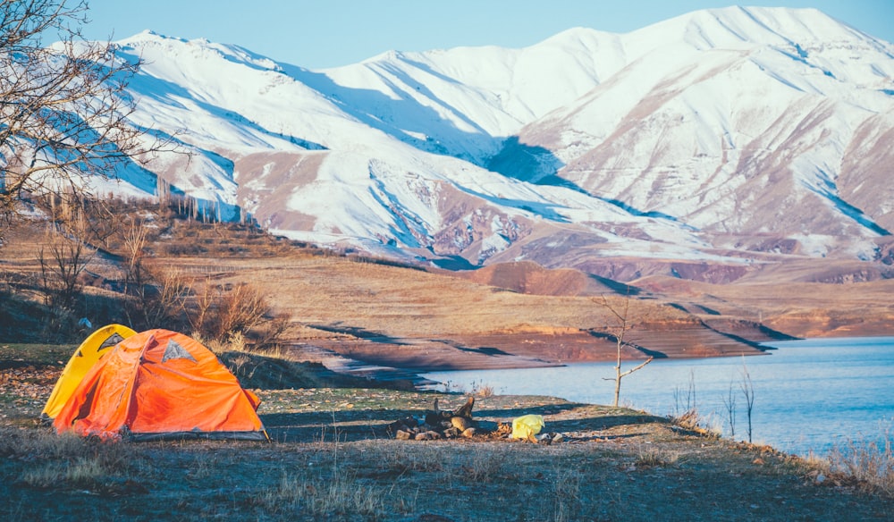 orange camping tent near body of water viewing mountain during daytime