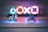 Two small toy figures resembling iconic movie characters ride motorcycles on a reflective surface. Illuminated gaming console symbols in vibrant colors are blurred in the background, creating a playful yet dynamic atmosphere in the dimly lit setting.