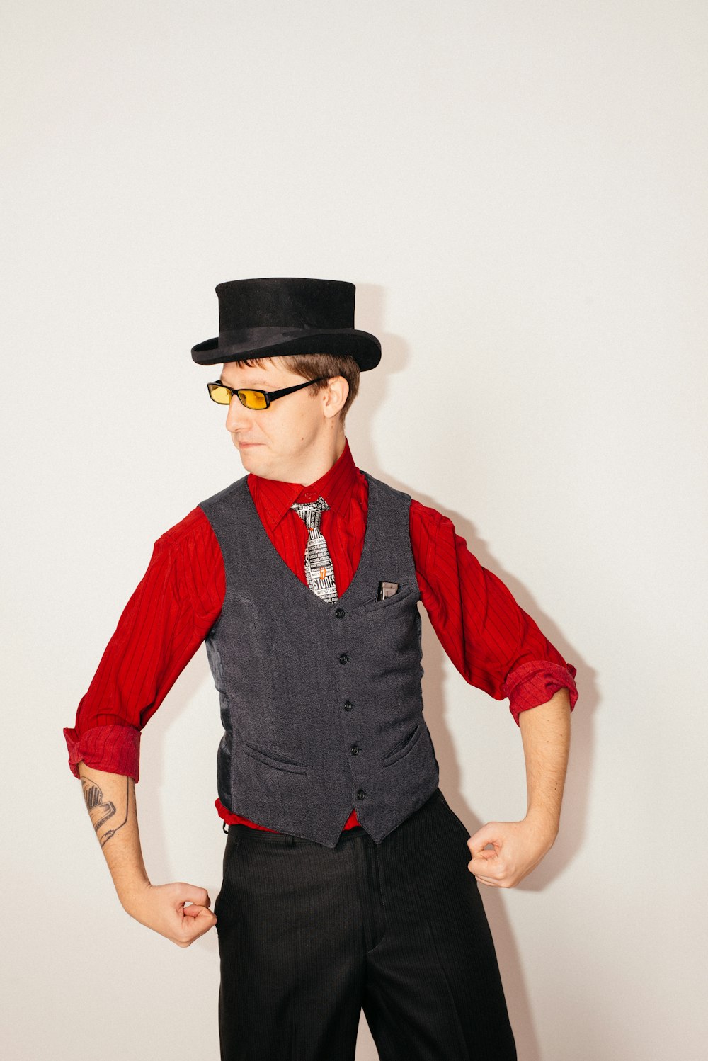 Foto hombre vestido con camisa de manga larga abotonada con cuello rojo,  chaleco gris y sombrero negro de pie mientras mira su lado derecho – Imagen  Vestir gratis en Unsplash