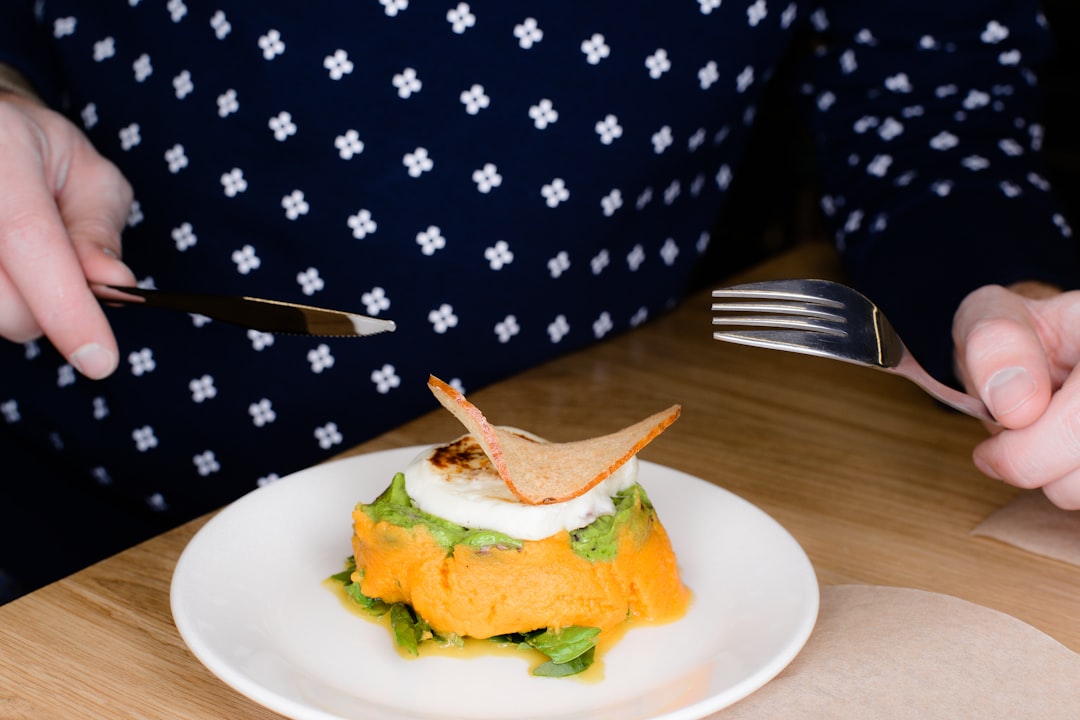 food on plate beside person holding fork and knife