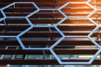 Geometric patterns of hexagons made from metal or plastic align parallel to a series of horizontal slats, possibly forming part of a building façade with a modern architectural design.