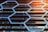 Geometric patterns of hexagons made from metal or plastic align parallel to a series of horizontal slats, possibly forming part of a building façade with a modern architectural design.