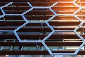 Geometric patterns of hexagons made from metal or plastic align parallel to a series of horizontal slats, possibly forming part of a building façade with a modern architectural design.