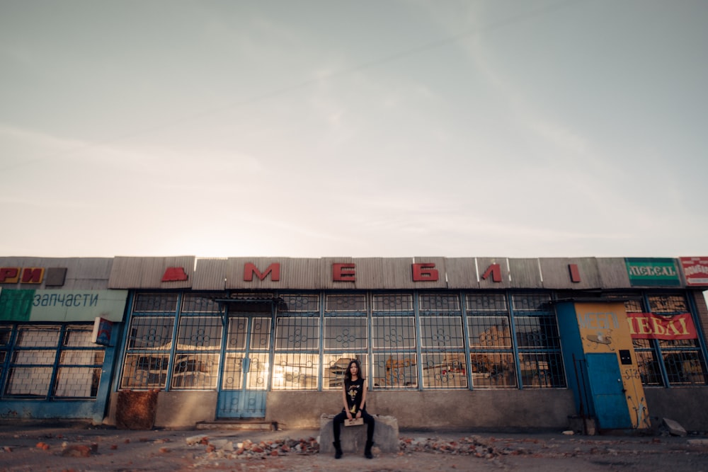 woman sitting near building under white and blue sky