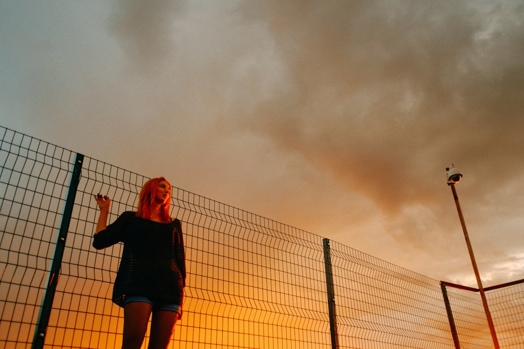 selective focus photography of woman beside fence during golden hour
