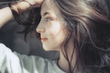 A side profile of a woman with long, flowing hair looking thoughtfully into the distance. The lighting highlights her facial features, and she appears to be deep in thought or contemplation.