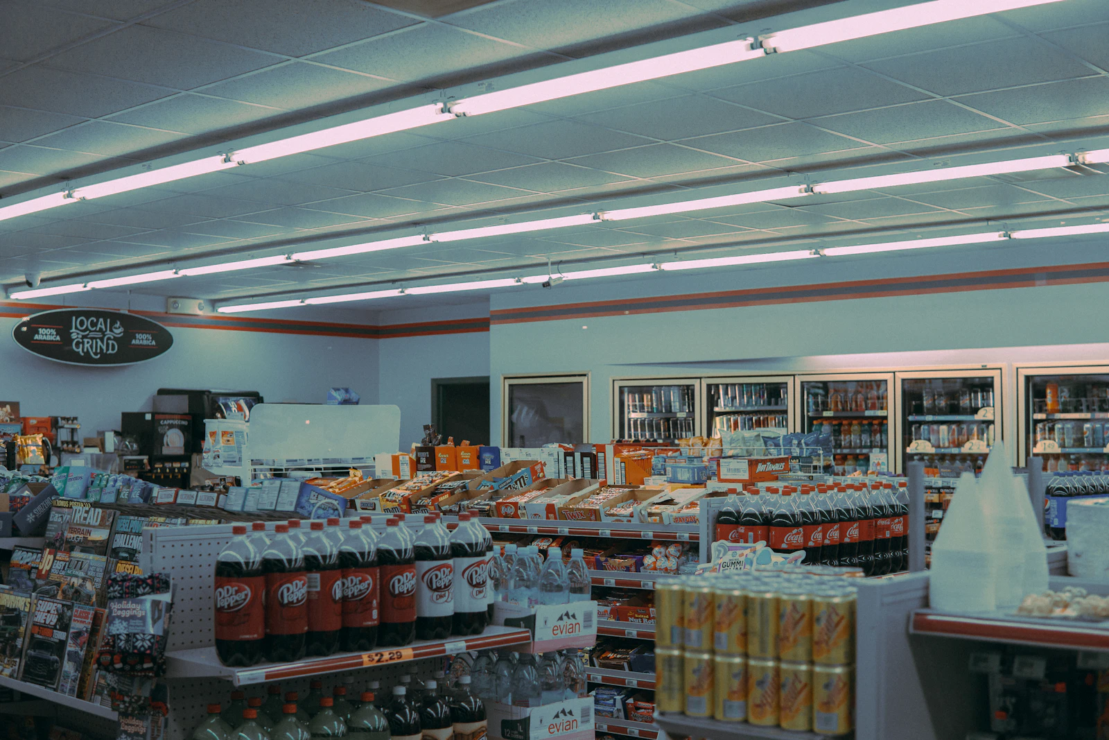 The lit interior of a small convenience store at night, with stocked shelves running back from the counter
