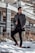 A well-dressed man in a long coat standing confidently in an urban setting.