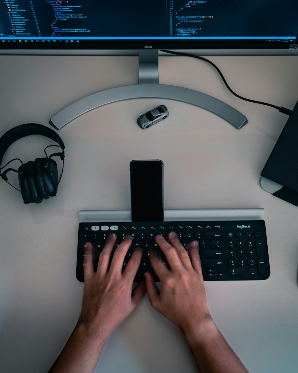 black and gray Logitech wireless keyboard with smartphone beside headphones and flat screen monitor