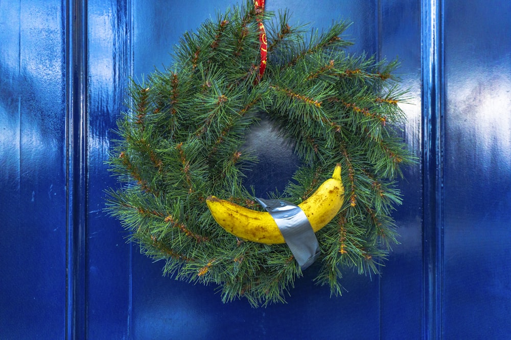 青いドアに黄色いバナナがぶら下がっている緑のトウヒの花輪