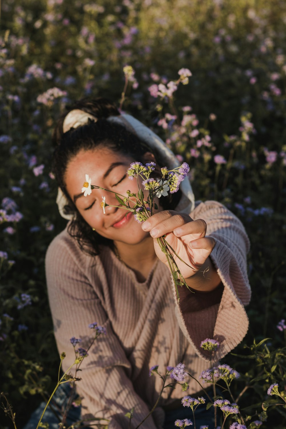 woman in gray sweater holding flowers outdoors