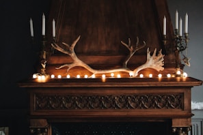 The fireplace mantle decorated with small plants and warm-toned candles casting gentle shadows.